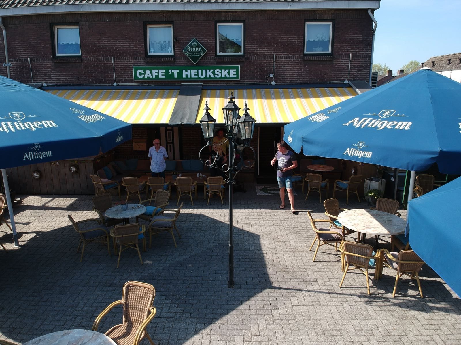 Het terras aan de voorkant met parasols en het naambord Cafe ’t Heukske