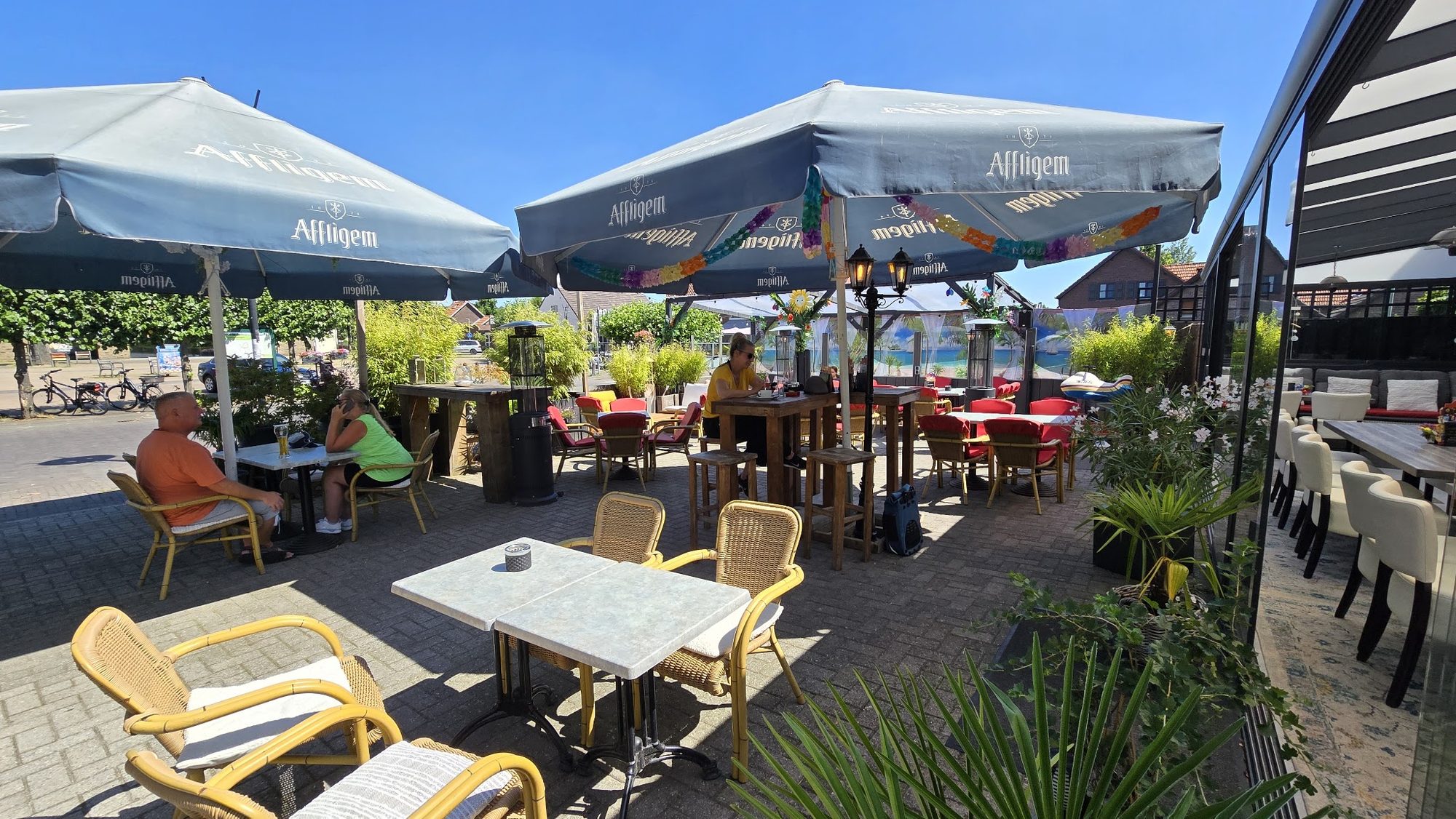 Het zonnige terras van ’t Heukske met parasols, rieten stoelen en veel groen